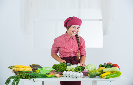 Lets cook it. kid wearing professional chef uniform. child in cook hat and apron. girl at kitchen. healthy organic food. diet and vitamin. happy childhood. happy teen girl cooking vegetables.