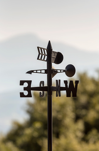 The contemporary, metallic, meteorological device weather vane against the background of forest and mountains close-up
