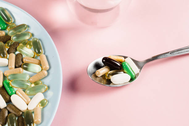 wiele suplementów diety tabletek, szklanka wody i łyżka do codziennego przyjmowania tabletek na różowym tle. zestaw tabletek, przeciwutleniaczy ze starzenia, lecytyny i adaptogenu. - vitamin pill nutritional supplement capsule lecithin zdjęcia i obrazy z banku zdjęć