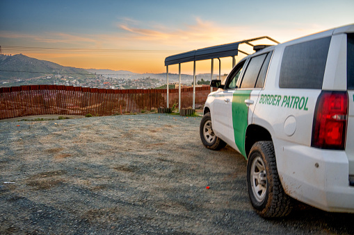 U.S. Border Patrol Official Vehicle Parked Near the International Border Barrier Wall Between the United States and Mexico in Tecate California at Dusk With Pretty Cloudscape, Observing Possible Illegal Migration Activity, or Smuggling