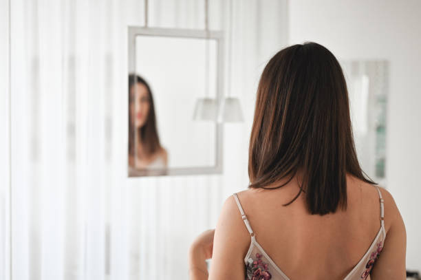 vista de trás mulher adulta média olhando para si mesma no espelho pela manhã. - rear view mirror - fotografias e filmes do acervo