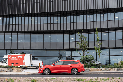 Gothenburg, Sweden - August 28 2022: Red car parked by a modern office building.