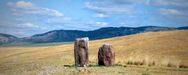 Photo of Two ancient menhirs with ribbons tied stand like guards in the endless steppe. Gates to the Valley of the Kings, Salbyk Steppe, Khakassia, South Siberia, Russia.