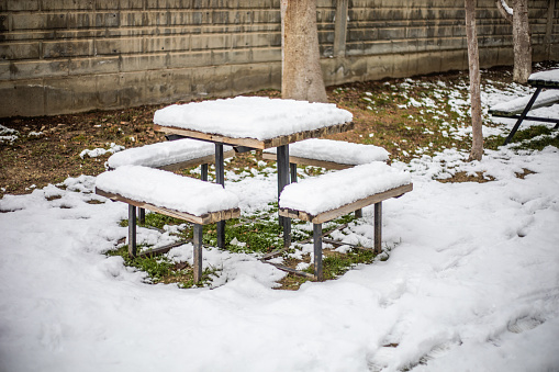 snowy weather picnic benches, snow mass has accumulated on the benches. The ground is grass but covered with snow. A cold winter day.