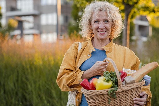 Portrait of a cheerful housewife holding a basket with groceries and looking at the camera. Healthy purchase.