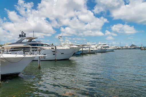 Row of boats tied on dock piles at Miami, Florida bay. Marina with white private boats against the puffy clouds in the sky background.