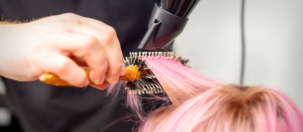 미용실에서 남성 미용사의 손에 의해 검은 헤어 드라이어와 검은 둥근 브러시로 젊은 백인 여성의 짧은 분홍색 머리를 말리고 닫습니다. - frizzy human hair hairdresser hair dryer 뉴스 사진 이미지