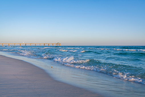 FORT WALTON BEACH, FLORIDA - CIRCA APRIL, 2022: Stunning sunset landscape with Okaloosa Island Pier. The famous fishing pier overlooks the vast sea with big waves against setting sun in the horizon.