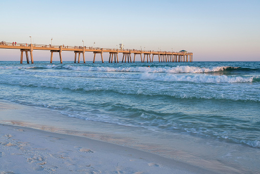 FORT WALTON BEACH, FLORIDA - CIRCA APRIL, 2022: Okaloosa isaland pier against setting sun and ocean. The fishing pier has a beautiful view of the sea with waves crashing on the shore at sunset.