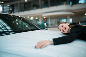Beautiful woman hugging and showing her love to a car at auto dealership