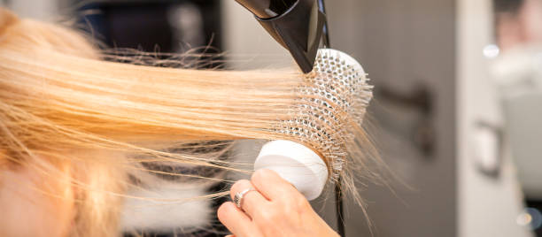 美容院で黒いドライヤーと白い丸いブラシでストレートブロンドの髪を乾かし、接写。 - frizzy human hair hairdresser hair dryer ストックフォトと画像