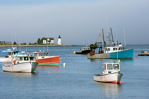 Colorful fishing boats in Inner Harbor and Prospect Harbor Point lighthouse, Maine Atlantic shore, USA