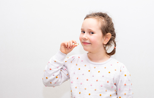 Portrait of a Caucasian girl, the child holds omega-3 gelatin pills in his hands and wants to take the pills. Girl on a gray background.