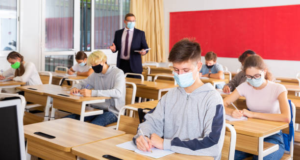 istock Teenagers in protective masks studying in classroom with teacher 1464594682