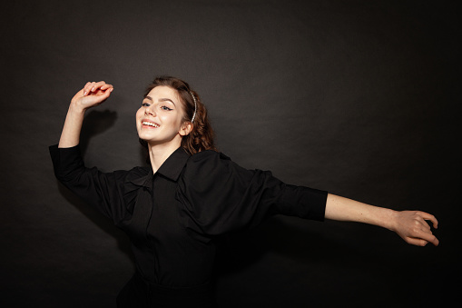 Studio portrait of happy dancing 20 year old white woman with brown curly hair against a black background