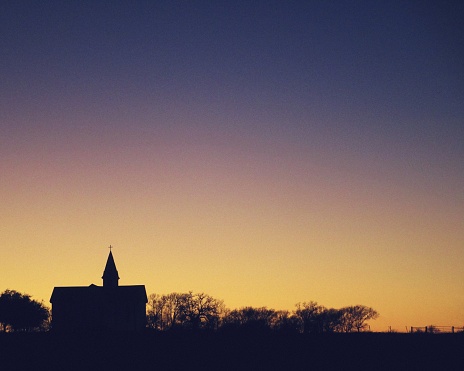 A rural church steeple, silhouetted against a winter twilight sky along a horizon in central Texas.