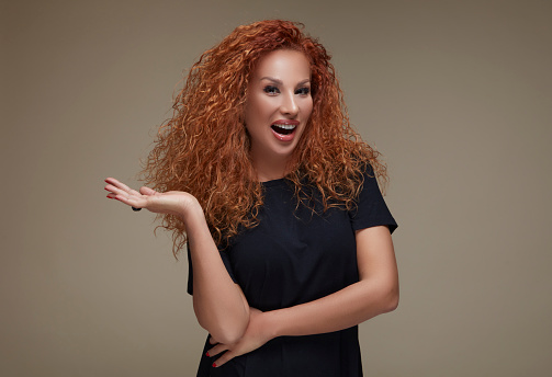 Smiling curly red-haired woman pretending to hold something in her right palm.