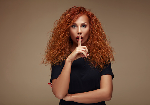 Red and curly hair woman making silence sign in fear.