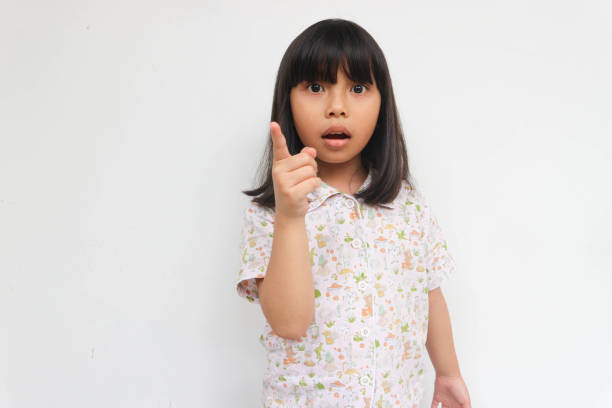 istock Surprised little girl wearing pajama looking at camera while pointing with hand, isolated on the grey background 1464603515
