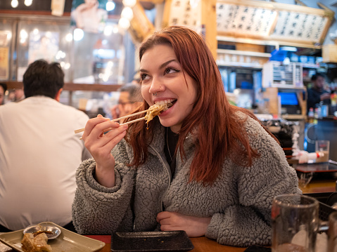 Happy young female tourist eating gyoza in Japanese Izakaya bar