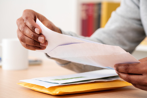 Close up of black man hands putting a letter inside an envelope on a desk at home or office