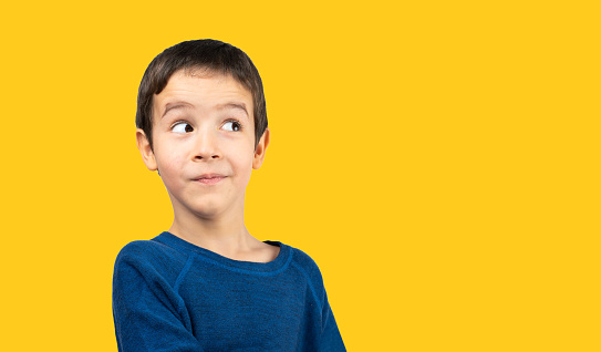 Dark haired little child with blue shirt over isolated yellow background looking away to side with smile on face, natural expression. Laughing confident.