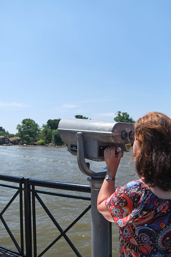 Latin mature woman viewing through public binoculars on the Lujan river bank in Tigre, Buenos Aires, Argentina.