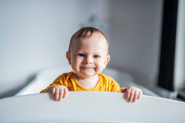 портрет милого маленького мальчика, заглядывающего в свою кроватку. - babies only стоковые фото и изображения