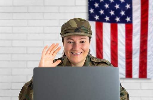Happy female soldier smiling cheerfully while video calling her family on a laptop. American servicewoman communicating with her loved ones while serving her country in the army.
