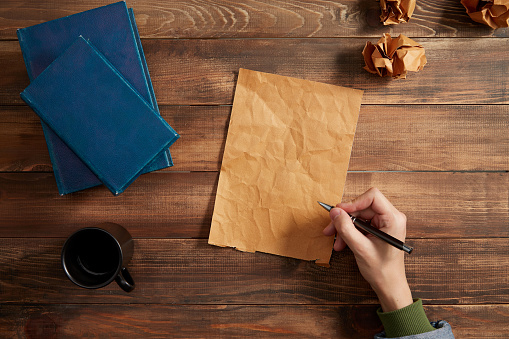 Writing on blank paper. Cup of coffee, book and crumpled paper on the wooden table.