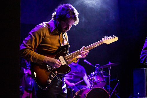 Rock band performs on stage. Guitarist, bass guitar and drums. Guitarist in the foreground. Close-up.