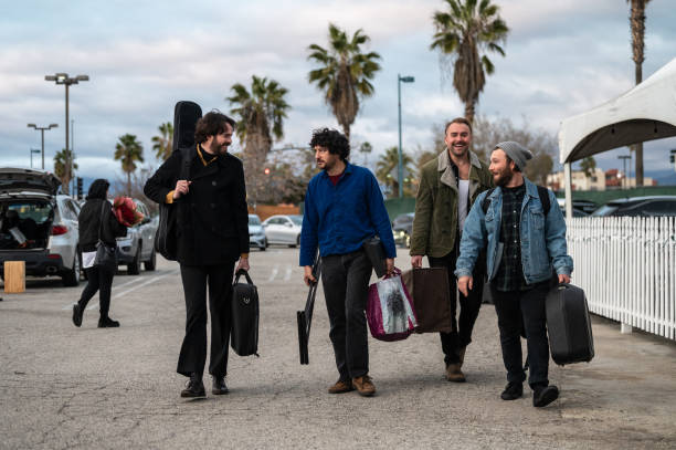 The members of a rock band carrying their instruments and equipment through the parking lot of a music venue before a show.