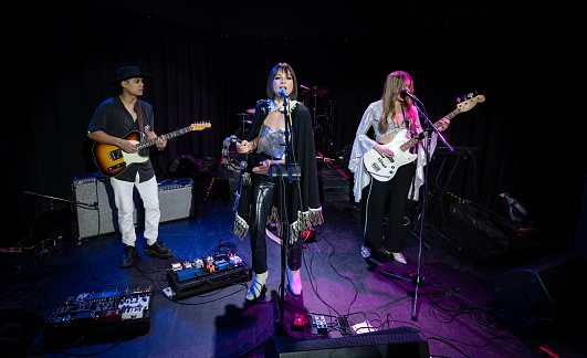 A female fronted rock band performing onstage at a music venue.