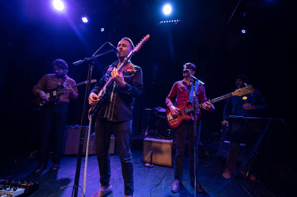 Singer Closing his Eyes While Performing Onstage with Band An Americana folk-rock band performing onstage in front of an audience at a live music venue. performance group stock pictures, royalty-free photos & images