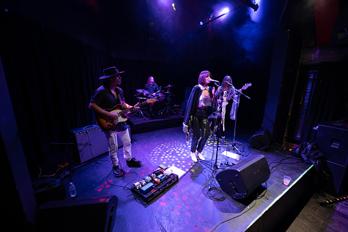 A female fronted rock band performing onstage at a music venue.