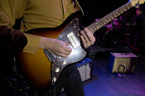 Close up on the hands of a man playing electric guitar onstage.