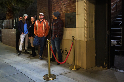A line of people wait behind a vervet rope to enter a music venue.