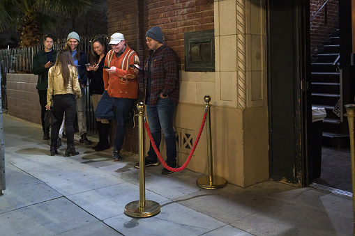 A line of people wait behind a vervet rope to enter a music venue.
