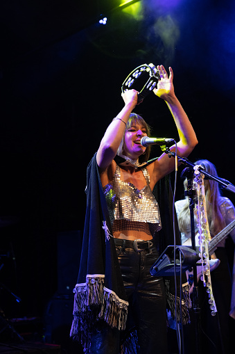 Woman singing on stage with a tambourine raised over her head.