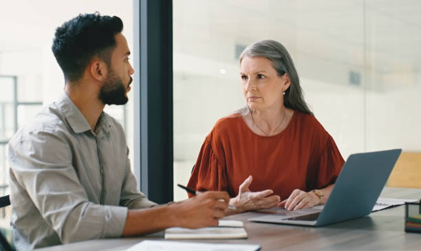 Collaboration of young businessman and senior woman in partnership in discussion or talking in office. Teamwork, project and diverse people working together for company or startup growth strategy stock photo
