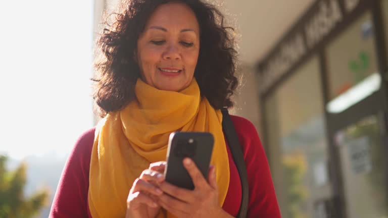 Cheerful Mature Latin American Female Checking Her Phone In The Street