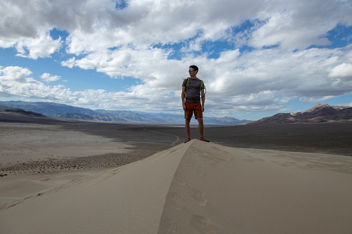 A male hiker stands atop the Eureka Dunes in Death Valley National Park, California. The Eureka Valley is seen in the background.