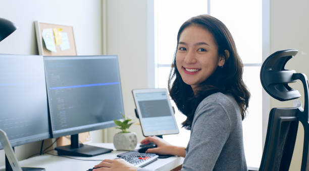 Portrait young Asian woman developer programmer, software engineer, IT support, look at camera and smile enjoy working at office. stock photo