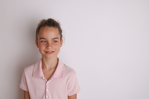 Little emotional teen girl in pink shirt 11, 12 years old on an isolated white background. Children's studio portrait. Place text, to copy space for inscription, advertising children's goods.