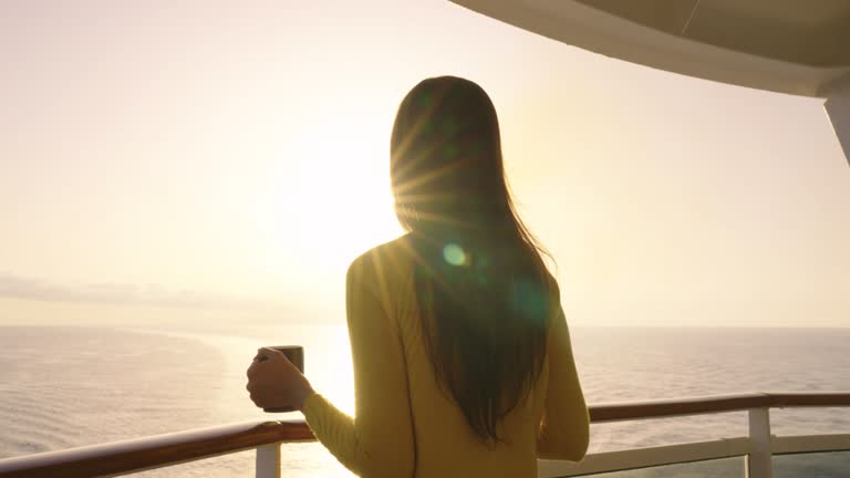 Cruise luxury travel lifestyle woman watching sunrise on private balcony deck and drinking coffee at the sunny morning.