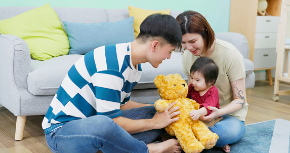 asian young father play toy bear stuffed animal with his child being embrace in mom arm