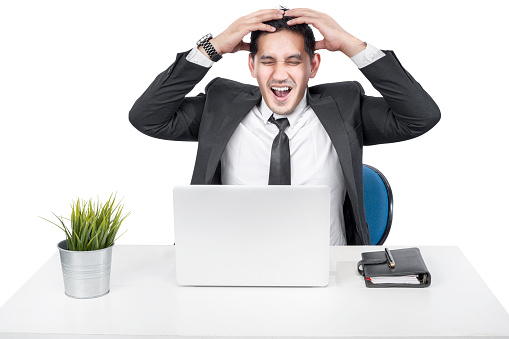 Asian businessman sitting with a laptop on the desk with a stressed expression isolated over white background