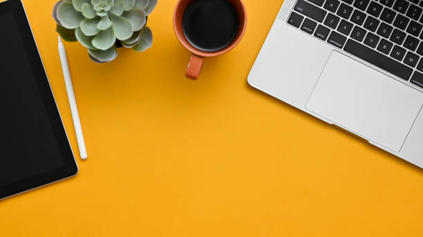 istock Top view of a creative workspace with laptop, coffee cup, tablet and copy space on yellow background 1464640200