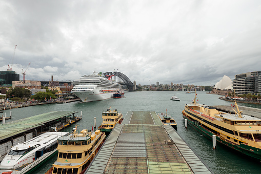 Sydney, Australia - February 9th, 2023: Sydney Harbor with Harbor Bridge, Opera House, Sydney Ferries, and Cruise ship “Carnival Splendor” moored. Overcast weather.