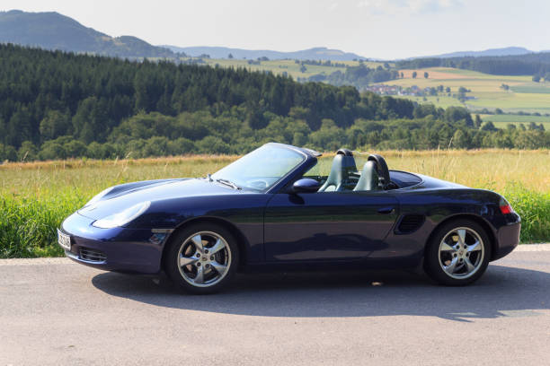 gersfeld, niemcy - 23 lipca 2021 r.: niebieski roadster porsche boxster 986 z panoramą gór rhön. samochód to dwumiejscowy samochód sportowy z silnikiem umieszczonym centralnie produkowany przez porsche. - germany landscape nissan roadster zdjęcia i obrazy z banku zdjęć